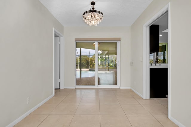 doorway with a textured ceiling, a sink, light tile patterned flooring, baseboards, and an inviting chandelier