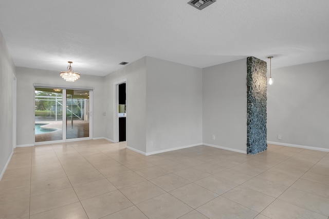 spare room featuring a textured ceiling, light tile patterned flooring, baseboards, an inviting chandelier, and visible vents