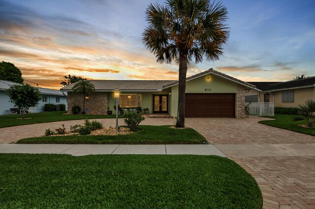 single story home with stucco siding, a yard, stone siding, and decorative driveway