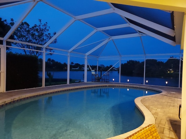 outdoor pool with glass enclosure, a water view, and a patio