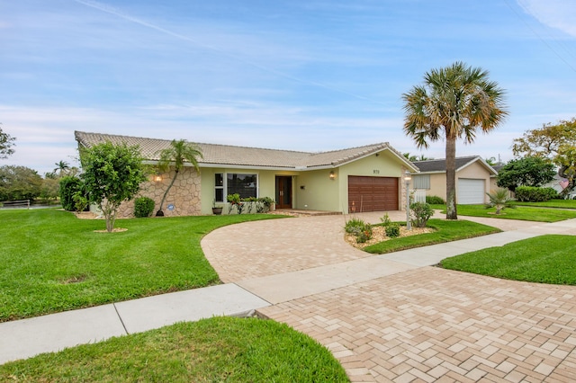 ranch-style home featuring a tile roof, a garage, a front yard, stucco siding, and decorative driveway