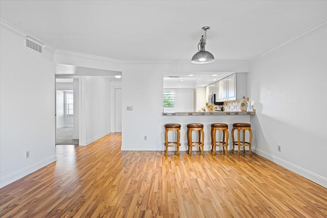 1811 SW Palm City Rd Unit A-202, Stuart, FL 34994 - kitchen featuring light wood-type flooring, a breakfast bar area, baseboards, crown molding, and hanging light fixtures