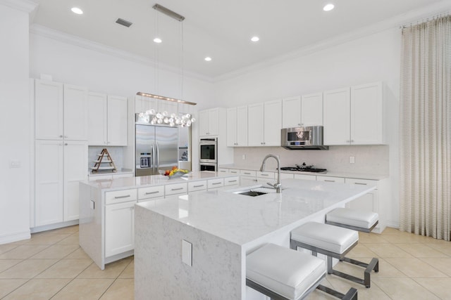 kitchen with appliances with stainless steel finishes, an island with sink, a sink, ornamental molding, and a high ceiling