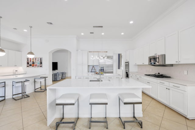 kitchen with appliances with stainless steel finishes, ornamental molding, a sink, light tile patterned floors, and a breakfast bar area