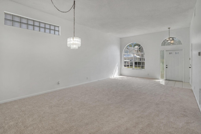 unfurnished living room with light carpet, a notable chandelier, and baseboards