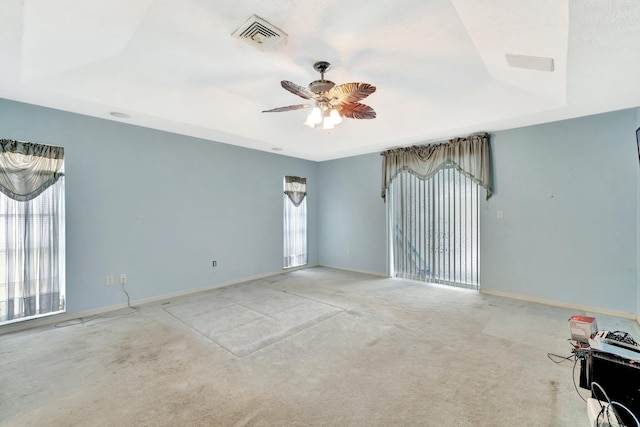 carpeted empty room with a raised ceiling, baseboards, a ceiling fan, and visible vents