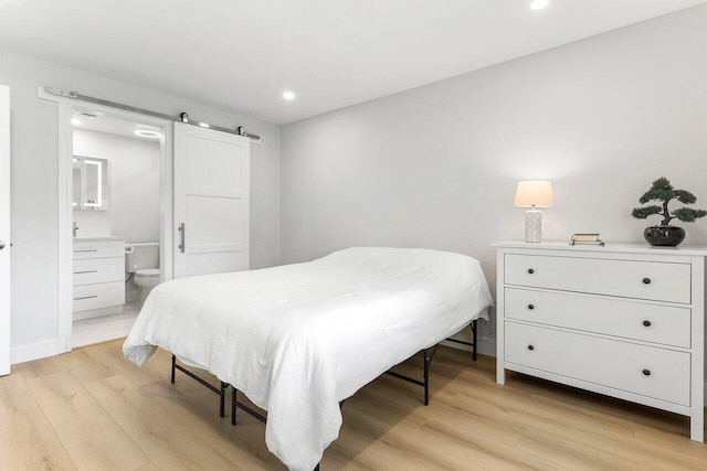 bedroom with recessed lighting, a barn door, light wood-style flooring, and ensuite bath