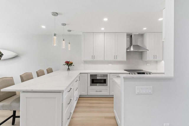 kitchen with tasteful backsplash, a peninsula, wall chimney range hood, white cabinetry, and a breakfast bar