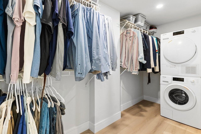 clothes washing area featuring laundry area, wood finished floors, stacked washer and clothes dryer, and baseboards