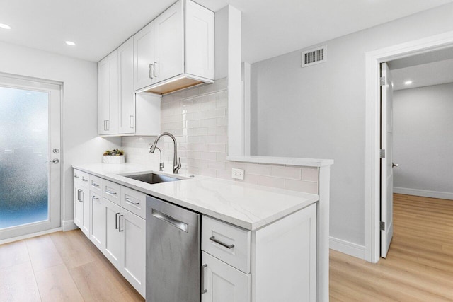 kitchen with stainless steel dishwasher, light wood finished floors, a sink, and backsplash