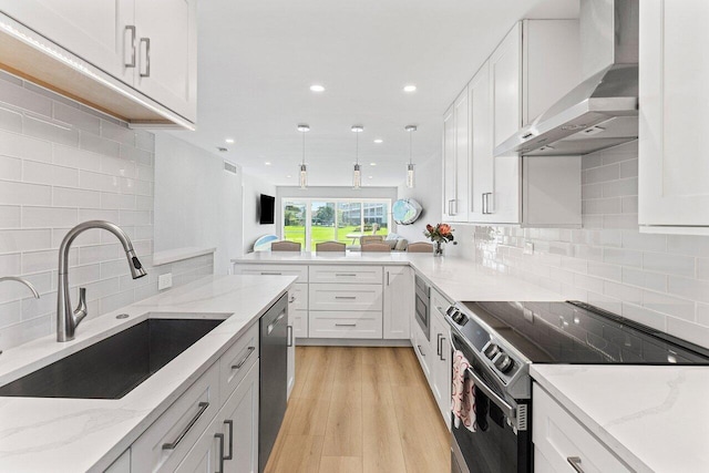 kitchen featuring tasteful backsplash, wall chimney range hood, light stone countertops, stainless steel appliances, and a sink