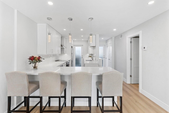 kitchen featuring a peninsula, light wood-type flooring, white cabinets, a sink, and a breakfast bar area