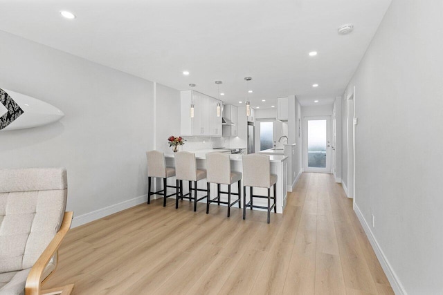 kitchen with light wood-style floors, white cabinetry, recessed lighting, light countertops, and a breakfast bar area