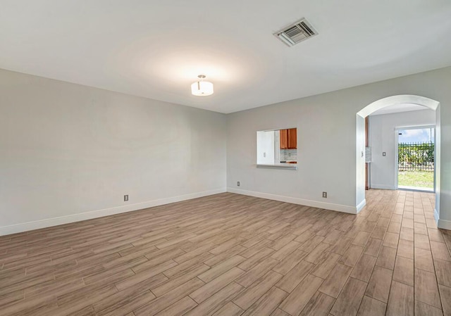 spare room with visible vents, baseboards, light wood-type flooring, and arched walkways