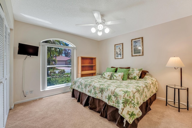 carpeted bedroom with a textured ceiling, a closet, a ceiling fan, and baseboards