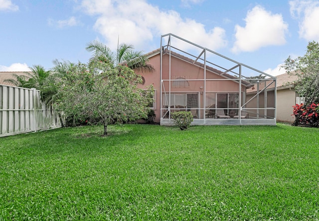 rear view of house with stucco siding, fence, a yard, and glass enclosure