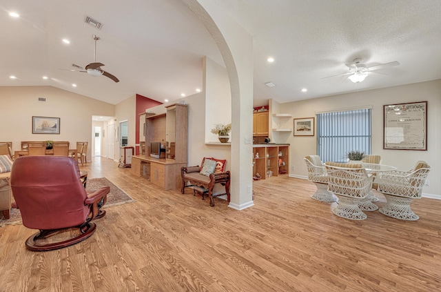living room with arched walkways, lofted ceiling, light wood finished floors, and ceiling fan