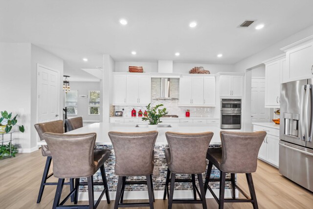 1104 Wandering Willow Way, Loxahatchee, FL 33470 - kitchen featuring wall chimney range hood, light countertops, a center island, stainless steel appliances, and white cabinetry