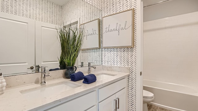 bathroom with wallpapered walls, double vanity, a sink, and toilet