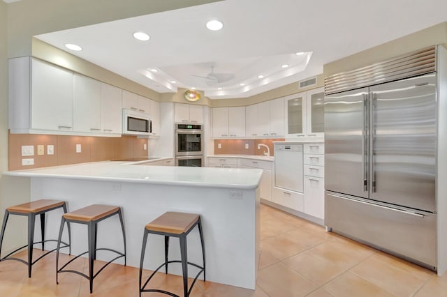 kitchen with a tray ceiling, recessed lighting, visible vents, a peninsula, and stainless steel appliances