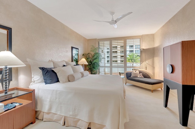bedroom with ceiling fan, light colored carpet, and a textured wall