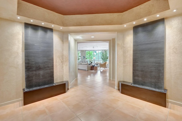 hallway featuring tile patterned floors, a tray ceiling, recessed lighting, and a textured wall