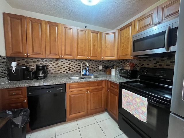 kitchen with light tile patterned floors, a sink, brown cabinetry, black appliances, and backsplash