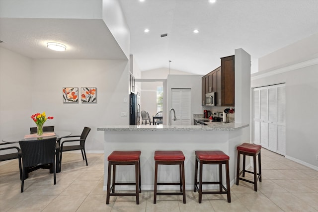 kitchen featuring lofted ceiling, light tile patterned floors, a breakfast bar area, appliances with stainless steel finishes, and dark brown cabinets