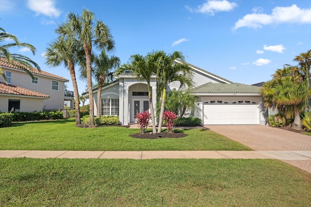 view of front of property with a front yard, stucco siding, decorative driveway, an attached garage, and french doors