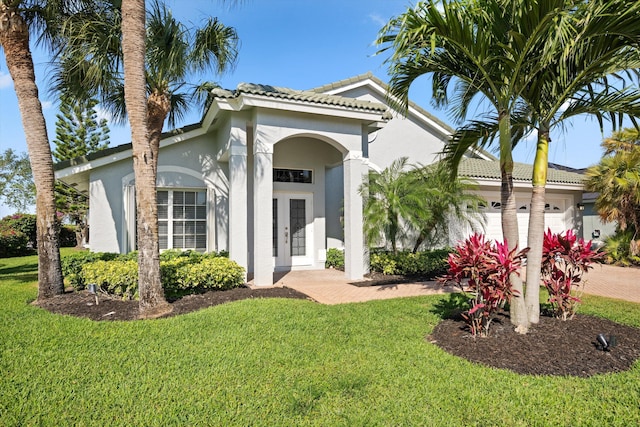 view of front of property with an attached garage, a tile roof, a front yard, and stucco siding