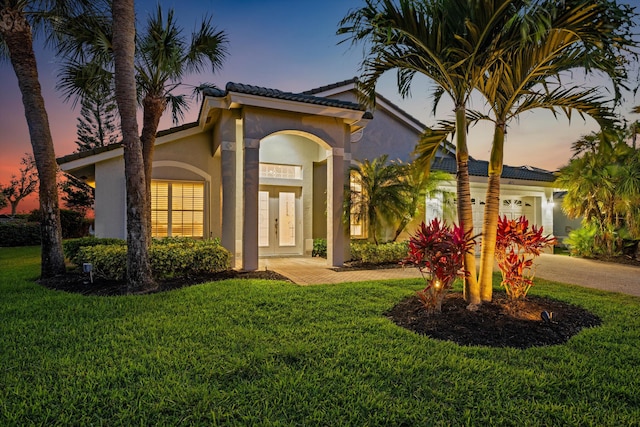 mediterranean / spanish-style house with a lawn, a tile roof, stucco siding, and a garage