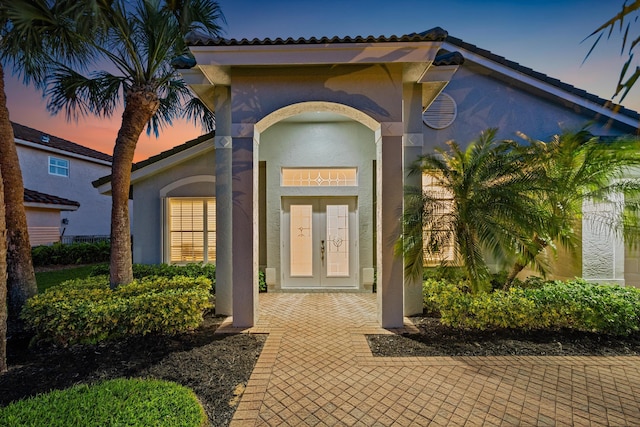 exterior entry at dusk with a tile roof and stucco siding
