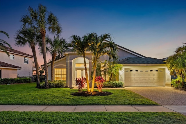 mediterranean / spanish home with a lawn, stucco siding, decorative driveway, and an attached garage