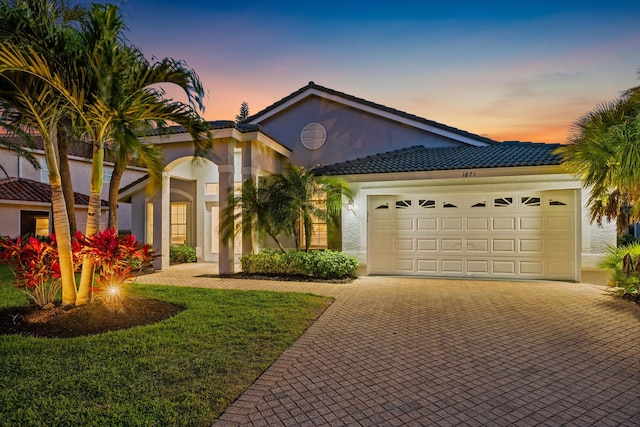 mediterranean / spanish-style home with stucco siding, a lawn, decorative driveway, a tiled roof, and an attached garage