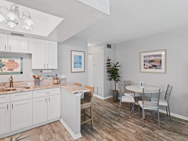 2800 Indian River Blvd Unit F8, Vero Beach, FL 32960 - kitchen with light wood-style flooring, white cabinets, light stone countertops, a peninsula, and a kitchen bar
