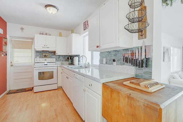 kitchen with a sink, light countertops, light wood finished floors, under cabinet range hood, and white appliances