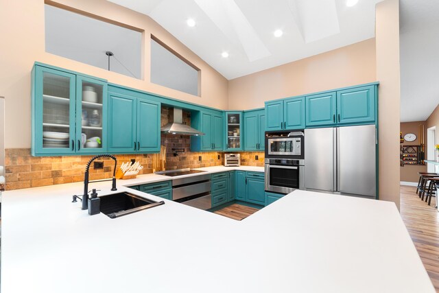 kitchen featuring a sink, light wood-style floors, wall chimney exhaust hood, stainless steel appliances, and decorative backsplash