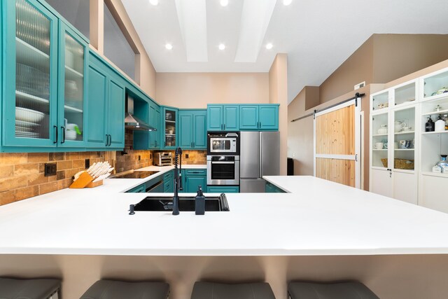 kitchen featuring appliances with stainless steel finishes, a barn door, wall chimney exhaust hood, a peninsula, and tasteful backsplash