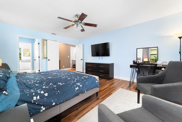 bedroom featuring ceiling fan, visible vents, wood finished floors, baseboards, and ensuite bath