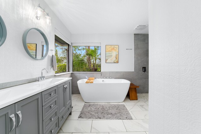 bathroom featuring tile walls, a soaking tub, vanity, and marble finish floor