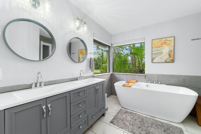 bathroom with double vanity, tile walls, a sink, and a freestanding bath