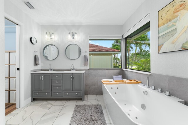 bathroom with a sink, a tub with jets, double vanity, and visible vents