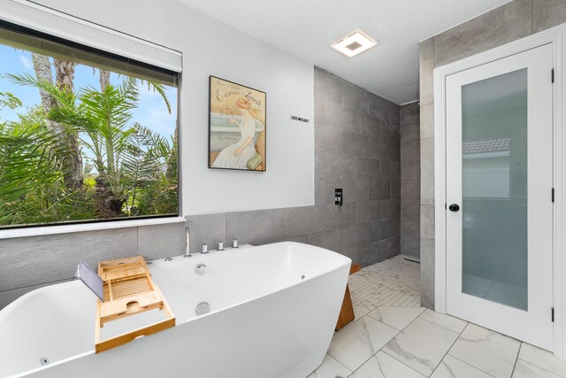full bath featuring a freestanding tub, tile walls, and marble finish floor