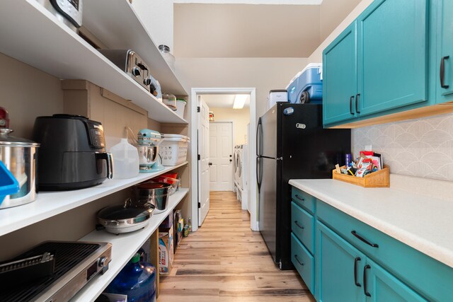 kitchen with backsplash, blue cabinetry, light countertops, freestanding refrigerator, and light wood-style flooring
