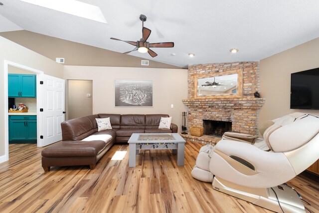 living area featuring light wood-type flooring, ceiling fan, vaulted ceiling with skylight, and a fireplace