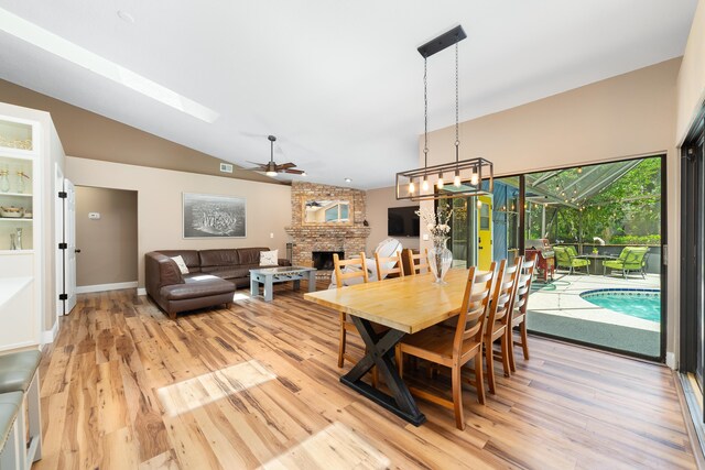 dining space featuring light wood-style floors, a brick fireplace, vaulted ceiling, and ceiling fan