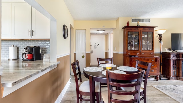 dining room featuring a textured ceiling, visible vents, baseboards, and light wood-style floors