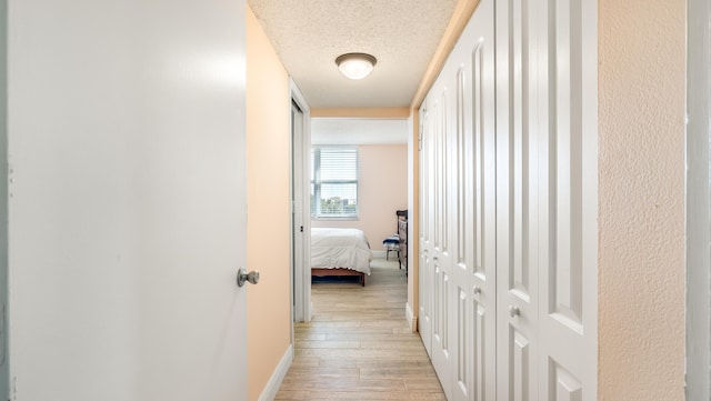 hallway with baseboards, light wood-type flooring, and a textured ceiling