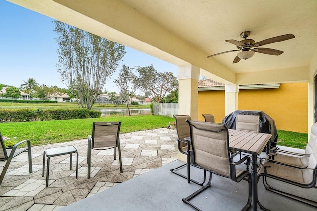 view of patio with fence, a ceiling fan, outdoor dining space, and a water view