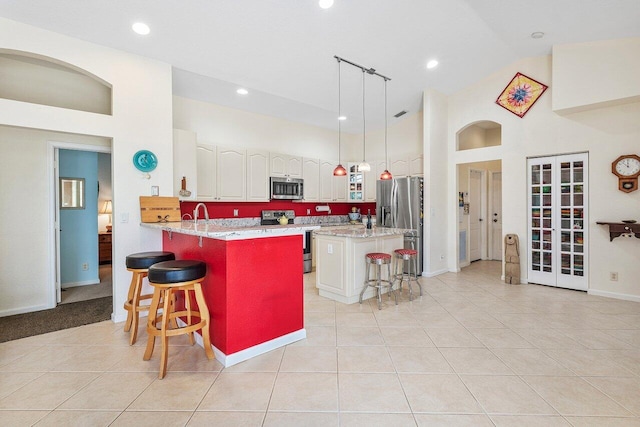 kitchen with high vaulted ceiling, light tile patterned flooring, a breakfast bar area, a peninsula, and appliances with stainless steel finishes